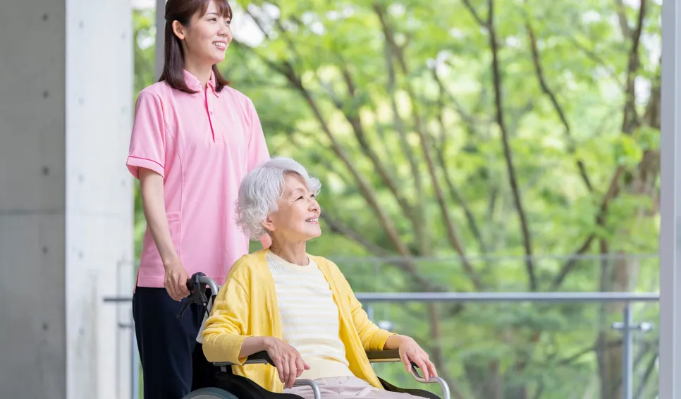 車いすの女性と介護スタッフが緑を眺める様子