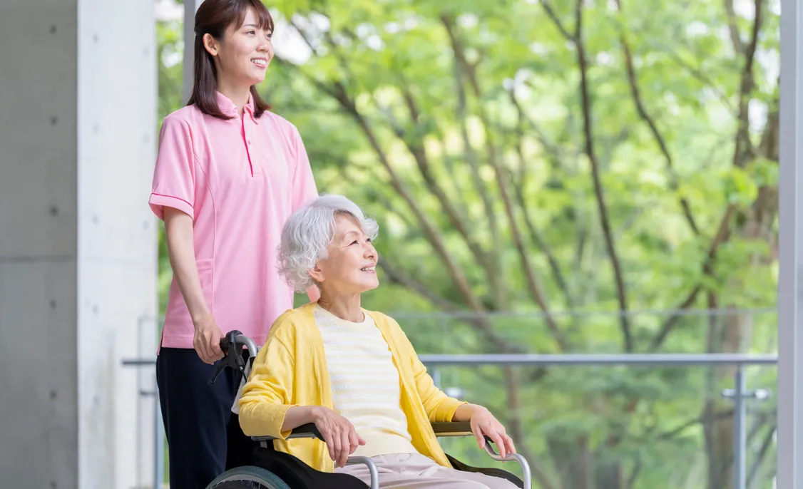 車いすの女性と介護スタッフが緑を眺める様子