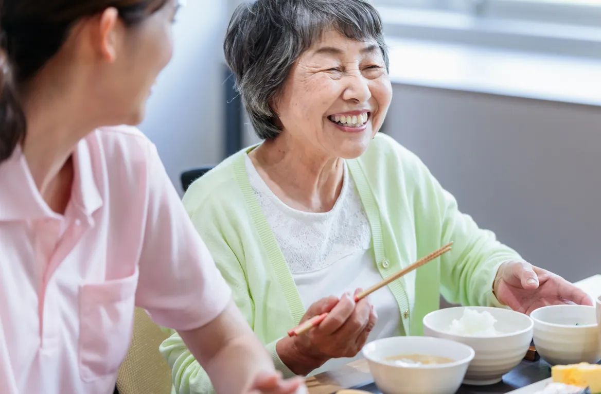 食事中に笑顔の高齢女性とスタッフ