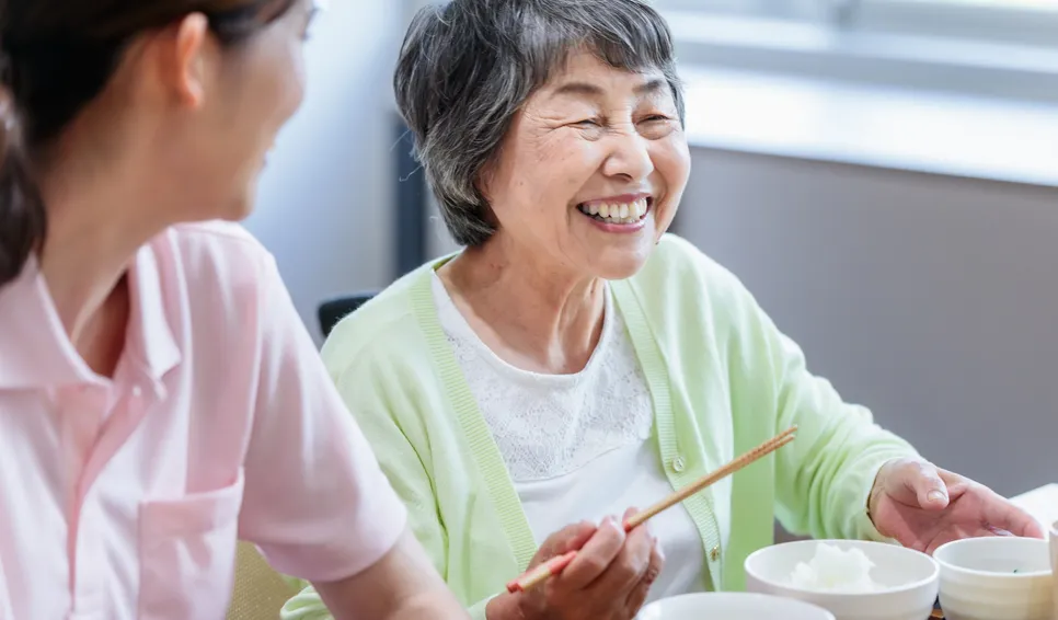 食事中に笑顔の高齢女性とスタッフ